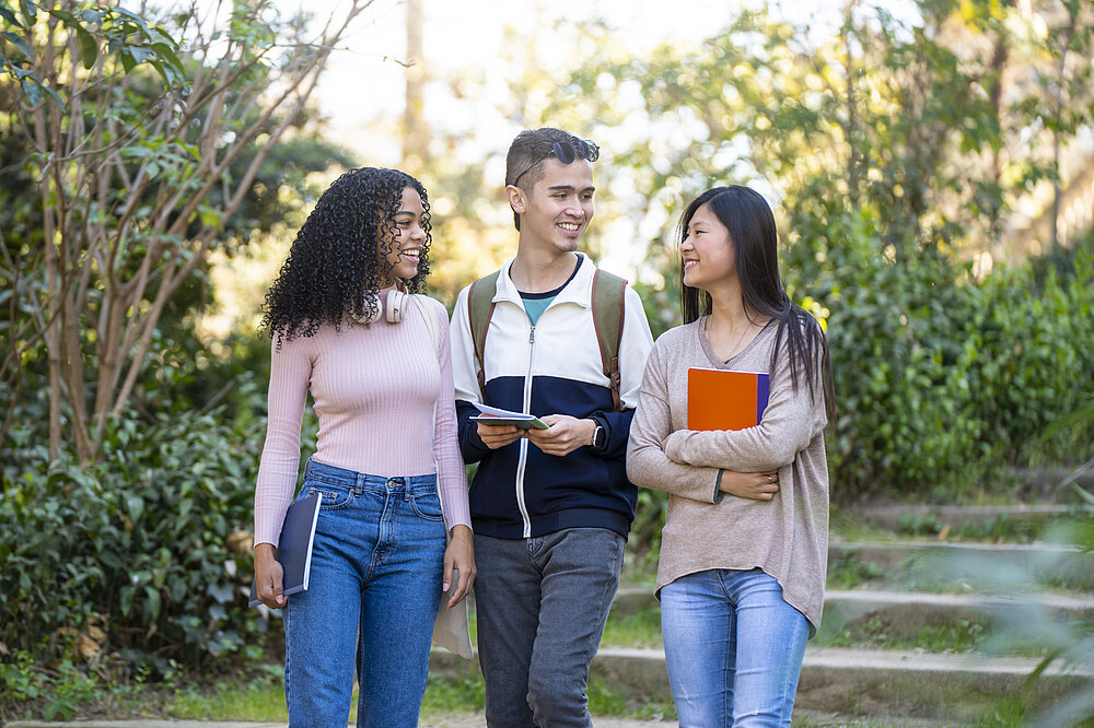 Three young multiethnic students walking in the street and talking. There are two women and one man